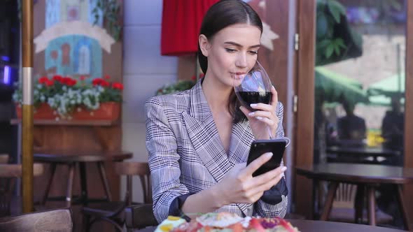 Smiling Woman Drinking Wine And Using Phone At Restaurant