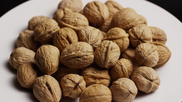 Cinematic, rotating shot of walnuts in their shells on a white surface - WALNUTS