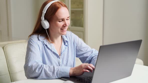 Woman with Headphones Works at Home on a Laptop Listens and Outlines a Lecture