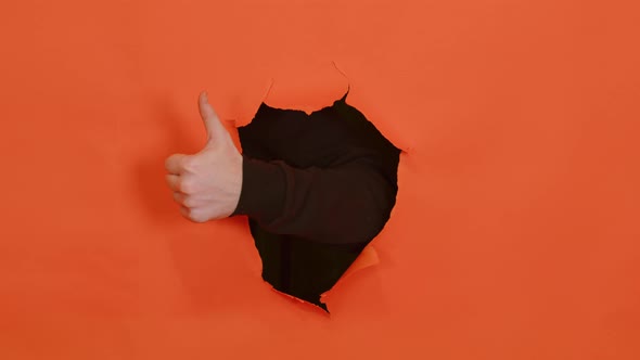 Man's Hand Showing Thumb Up and Sticking Out of Hole of Orange Background