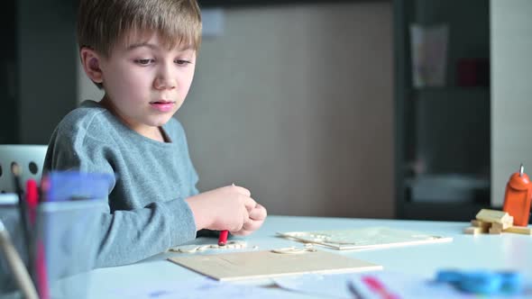 The child collects a wooden craft from parts, sitting in his room