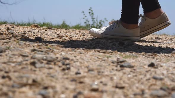 Female Feet of Hiker Goes on the Top of Cliff in Mountains. Legs of Girl in Sneakers Steps on the