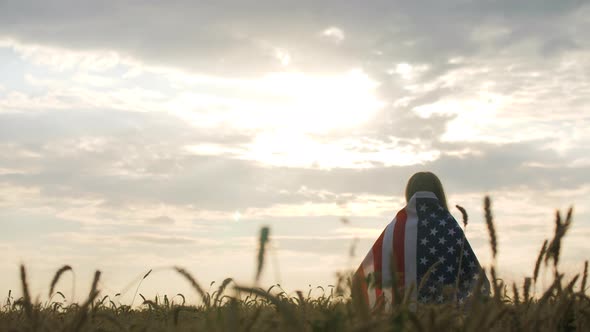 Patriotic Young Woman Stands in a Field Wrapped in the US Flag