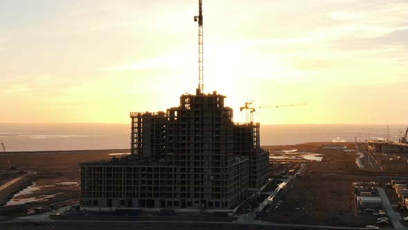 Flying Over the Construction Site, the Work of Construction Cranes and Workers at Sunset, Aerial