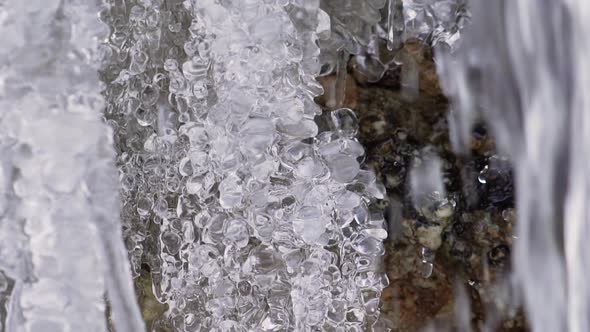 Meltwater cascading over frozen waterfall, macro closeup of winter stream