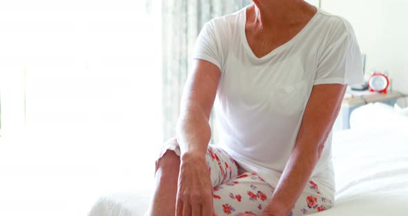 Thoughtful senior woman sitting on bed in bedroom