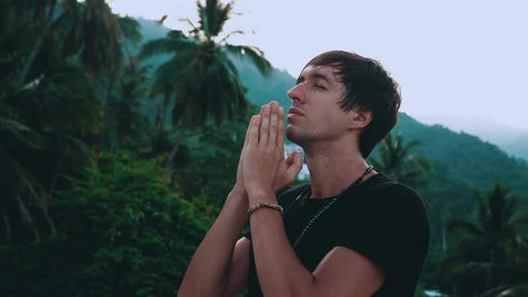 Profile of Pensive Man Holding Hands in Namaste Gesture Standing on Beautiful Jungle Nature with