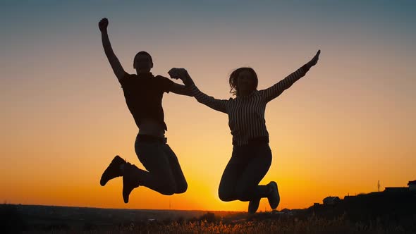 Cheerful Couple Jumping at Sunset