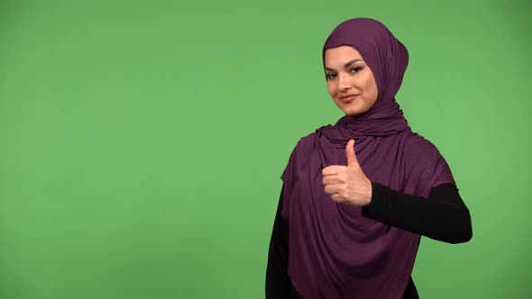A Young Beautiful Muslim Woman Shows a Thumb Up to the Camera with a Smile  Green Screen Background