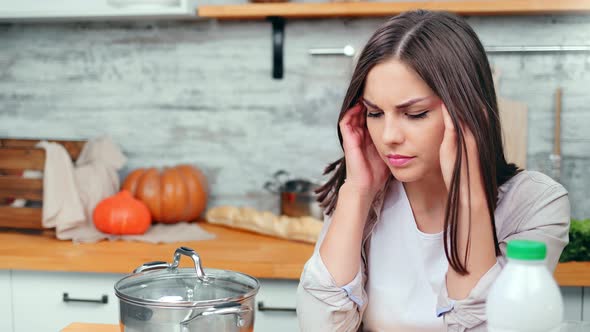 Unhappy Young Woman Housewife Having Headache Massaging Temple with Closed Eyes in Kitchen