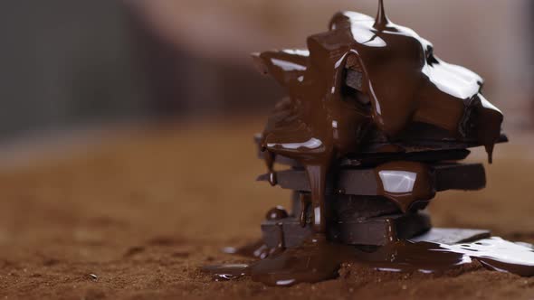 Melted Chocolate Pouring Over Stack of Dark Chocolate at Table with Cocoa Powder