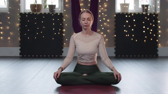 A Woman Sits on a Yoga Mat and Does Breathing Exercises