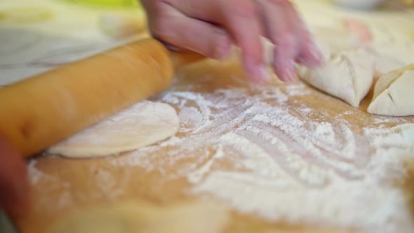 a Woman's Hand Rolls Out Pieces of Raw Dough in Flour with a Rolling Pin