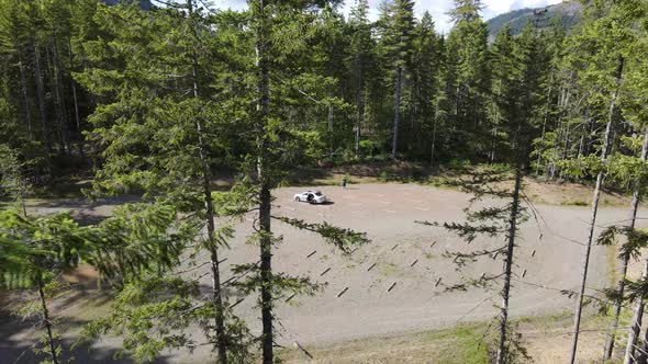 Man, silver car, parking lot flying backwards through green trees reveal natural lake mountain cloud