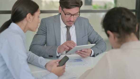 Middle Aged Businessman using Tablet and Female Colleague using Smartphone