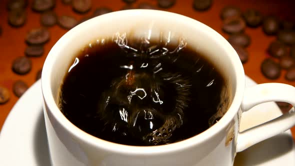 In Cup with Black Coffee Falls One Piece Sugar. Closeup