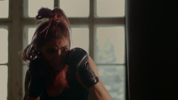 Athletic Fit Female Boxer Exercising Punches with Boxing Bag in Gym During Kickboxing