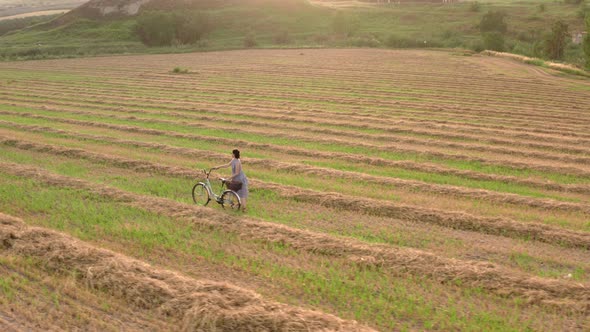 Girl Rides a Bicycle on a Rural Field in the Evening Before a Sunny Sunset,  Rows of Harvested Wheat