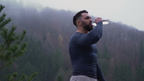 Young Bearded Man with Muscular Chest Drinking Water From Bottle After Training