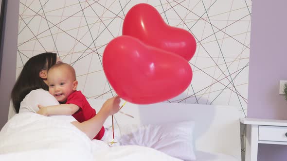 Pretty Young Female Mother Baby Toddler Kid White Bed Red Heart Balloons Holiday