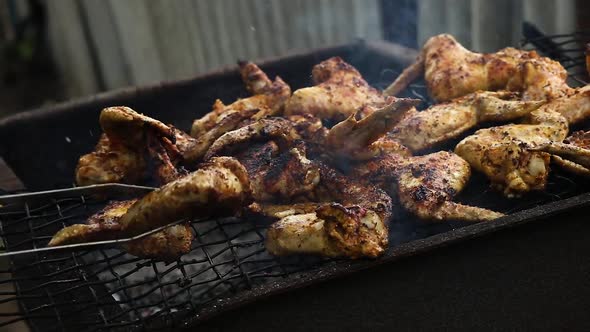 Man Using Metal Tongs To Turning Chicken Wings Which Are Being Grilled on Barbecue