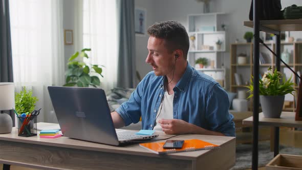 Young Man Talking on Video Calling in Headphones at His Laptop at Home in the Living Room