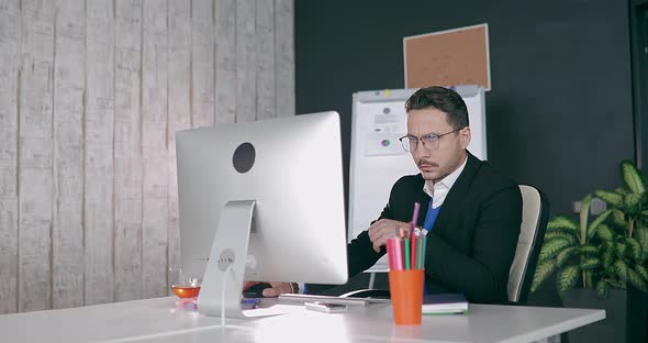 Businessman in Glasses Sits at Computer in Office