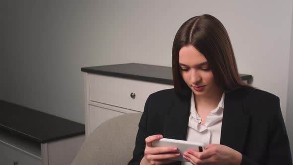Portrait of Young Woman Plays Mobile Game on Phone at Home or Office