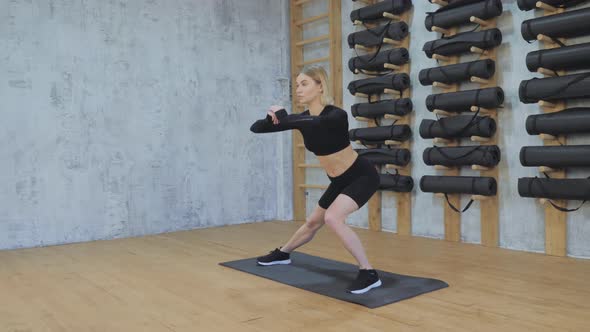 Young fit beautiful girl in black top, leggings, black sneakers doing leg joint stretching exercise