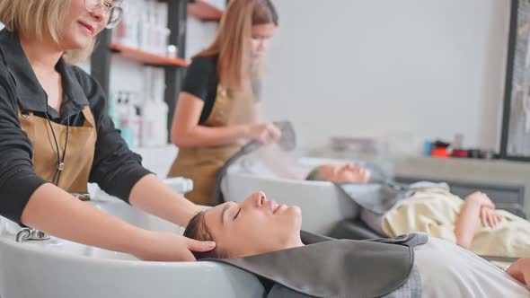 Group of young woman lying down on salon washing bed getting hair washed by hairdresser in salon.