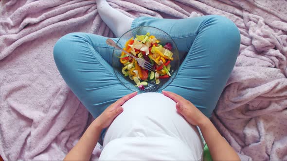 A Pregnant Girl Is Sitting in the Lotus Position and Stroking a Large Belly in a T-shirt, Between