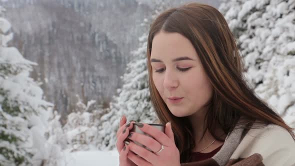 A Young Girl is Drinking Hot Tea in a Snowy Forest She is Warmed By a Drink From a Thermos