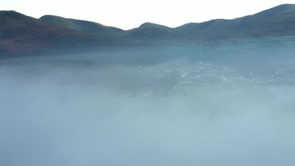 Aerial view of a lake and town covered by fog and clouds at sunset