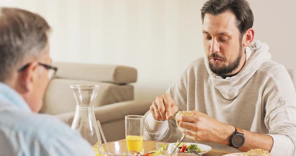 A Handsome Young Brunet Sits with His Father at the Table They Eat Breakfast Together