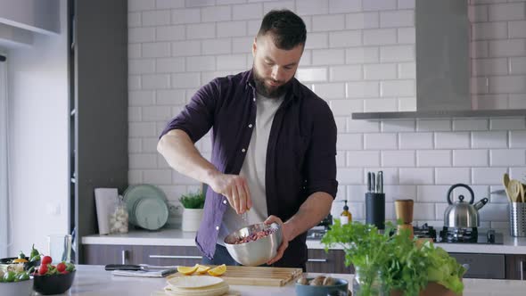 Young Man Cooking in the Kitchen, adding Lemon Dressing to Fresh Vegetables Salad