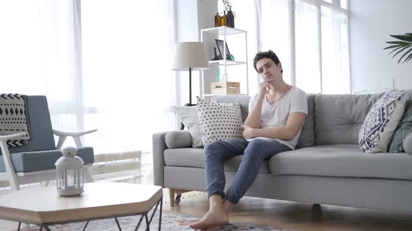 Pensive Young Man Thinking While Sitting on Sofa at Home