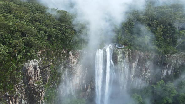 Cinematic view flying through fog clouds to reveal a majestic waterfall flowing into a tropical rain