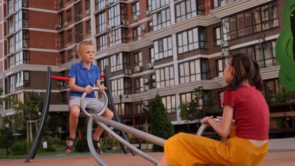 Two Cheerful Children are Riding on a Swing on the Playground in the Courtyard