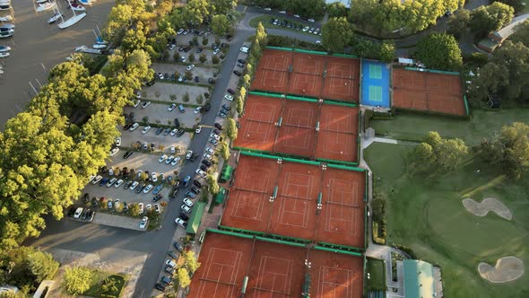 Aerial orbiting over clay tennis courts, a golf playground and a parking lot on a private sport club