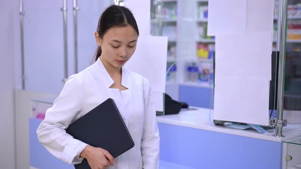 Female Asian Pharmacist Cashier Posing with Digital Tablet at Cash Desk in Drugstore