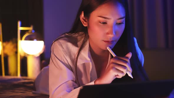 Young Asian beautiful woman enjoy using smartphone- tablet   in bedroom at night time.