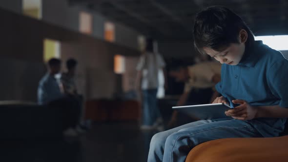 Teen Boy Sitting Holding Tablet in School Hall