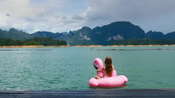 Back View of Woman on Vacation Sitting and Swimming on Pink Floating Flamingo