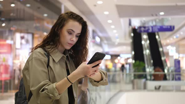 A Girl in a Shopping Mall Looks Sadly at the Screen of Her Phone