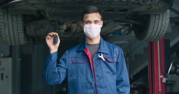 Young Mechanic in Protective Mask Showing Keys After Settling Car, Vehicle Ready To Start