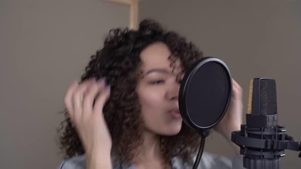 Young Woman Singer with Curly Hair is Recording a Song in a Recording Studio