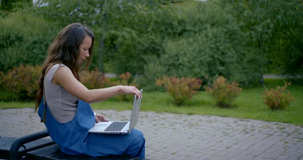 Pretty Brunette Opens Modern Laptop and Types in Park