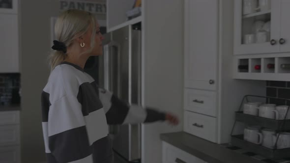 Woman walking up to a cabinet to grab a cup to make coffee.