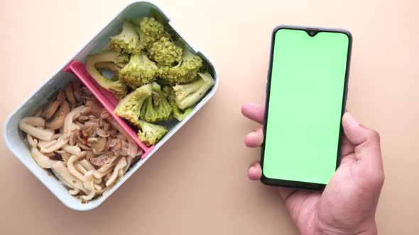 Top View of a Lunch Box and a Holding a Smart Phone