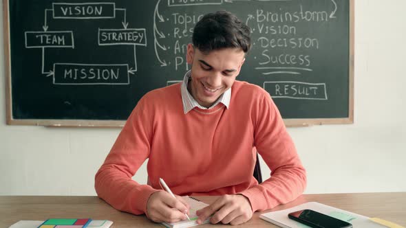 Happy Smiling Indian Student at Desk in Classroom Writing Notes